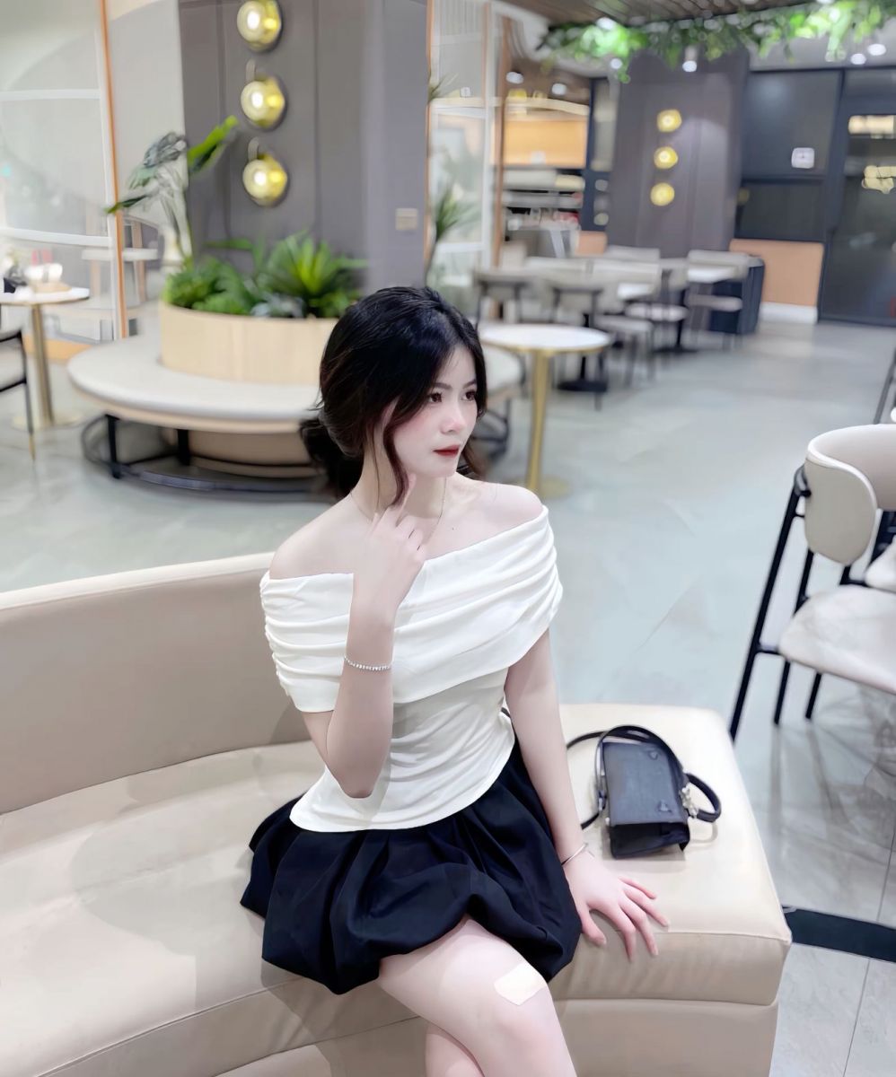 Ảnh gái mặc áo trắng cổ rộng và chân váy đen ngồi trên ghế sofa
