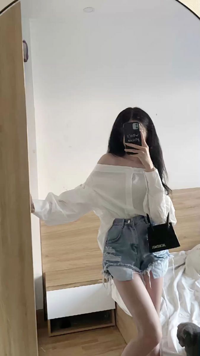 Cô gái mặc áo blouse trắng rộng và quần shorts jeans chụp ảnh trong gương