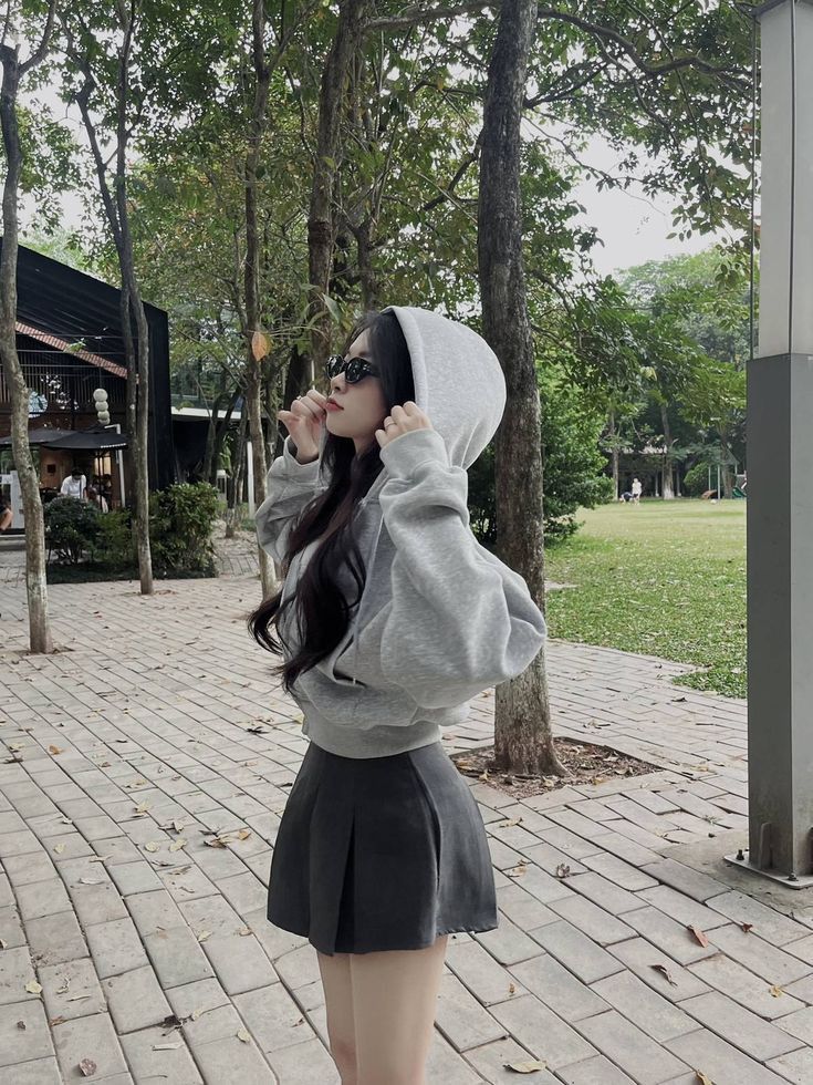 Cô gái mặc áo hoodie xám và chân váy đen giữa công viên