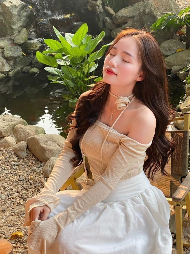 Cô gái mặc áo off-shoulder màu kem và chân váy trắng bên hồ