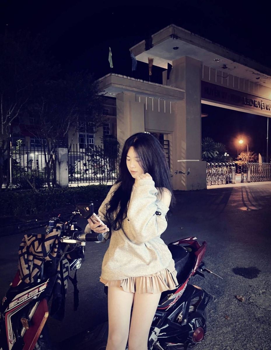 Cô gái mặc áo sweater và chân váy ngắn bên xe máy