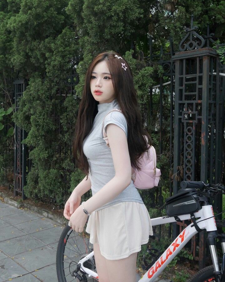 Cô gái mặc áo thun xám và chân váy ngắn màu trắng bên xe đạp