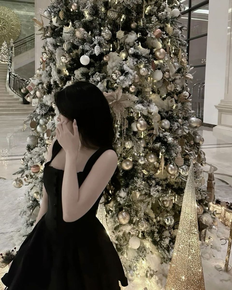 Cô gái mặc váy đen bên cây thông Noel rực rỡ