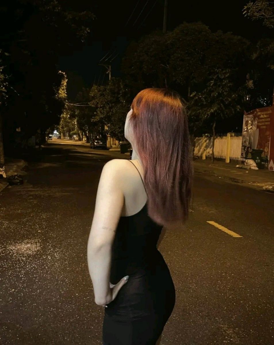Cô gái mặc váy đen đứng lưng lại giữa phố đêm vàng ánh đèn