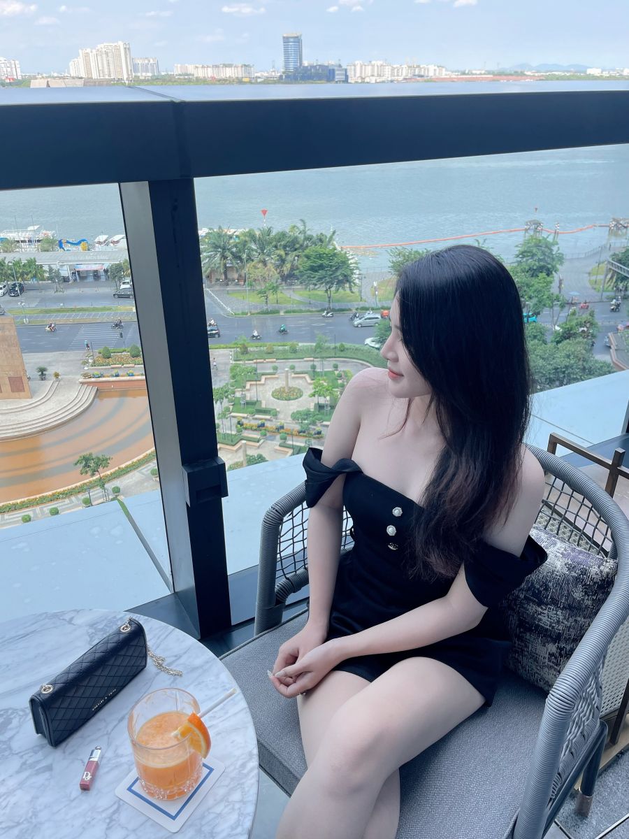 Cô gái mặc váy đen ngồi bên ban công nhìn ra sông