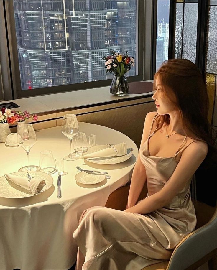 Cô gái mặc váy satin ngồi bên cửa sổ nhìn ra thành phố về đêm