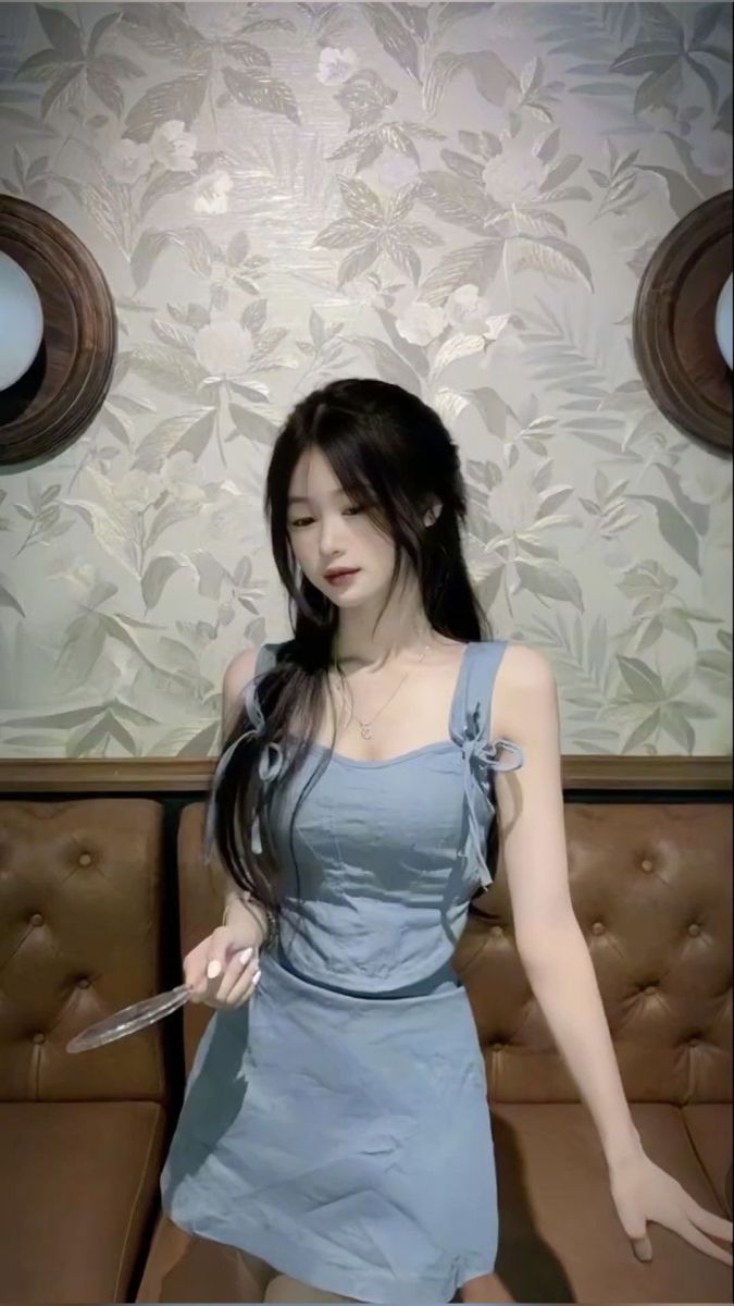 Cô gái mặc váy xanh nhạt đang ngồi thư giãn trên ghế đá cam