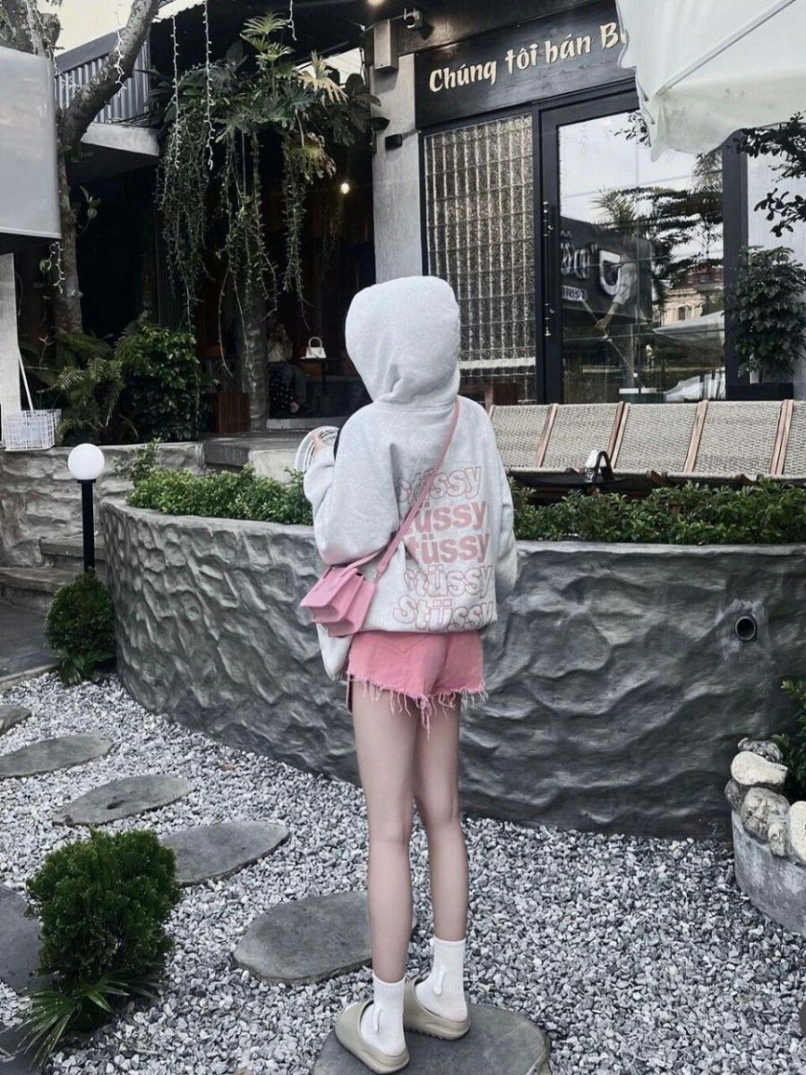 Cô gái trẻ diện hoodie xám và quần short hồng tại quán cà phê xinh xắn