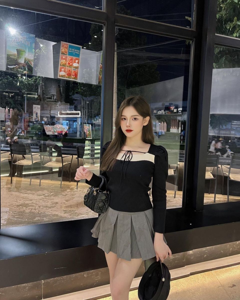 Cô gái trẻ mặc áo bệt vai màu đen và chân váy xếp ly xám