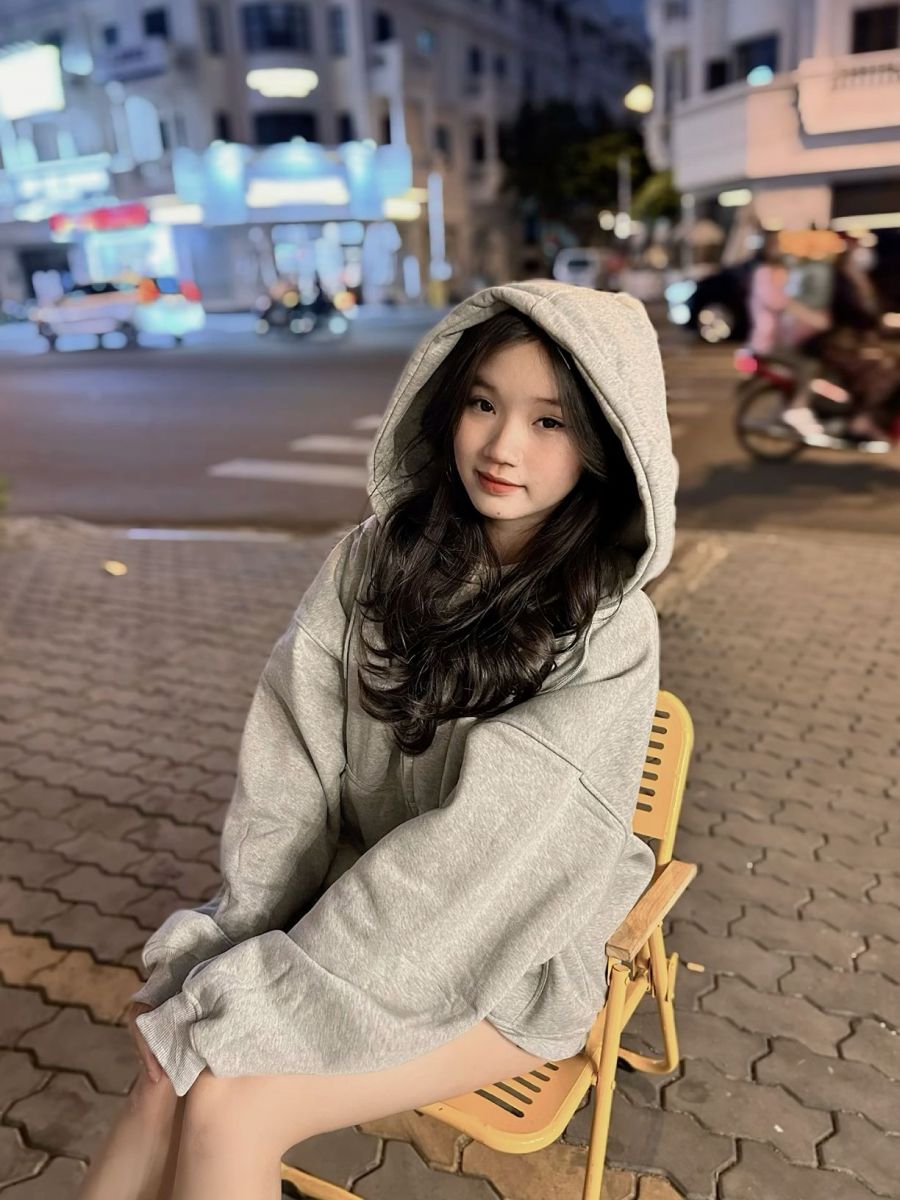 Cô gái trẻ mặc áo hoodies màu xám ngồi thư giãn tại phố vào buổi tối