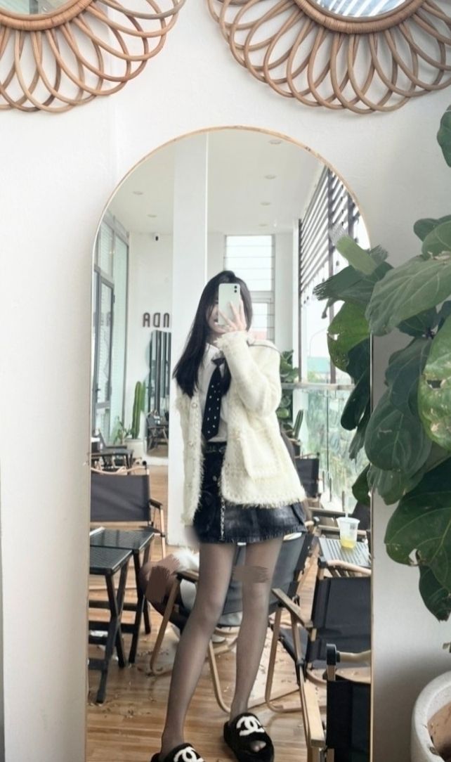 Cô gái trẻ mặc áo khoác lông và chân váy denim chụp ảnh trong gương