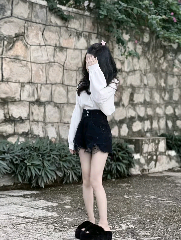 Cô gái trẻ mặc áo sơ mi trắng và chân váy denim đen che mặt