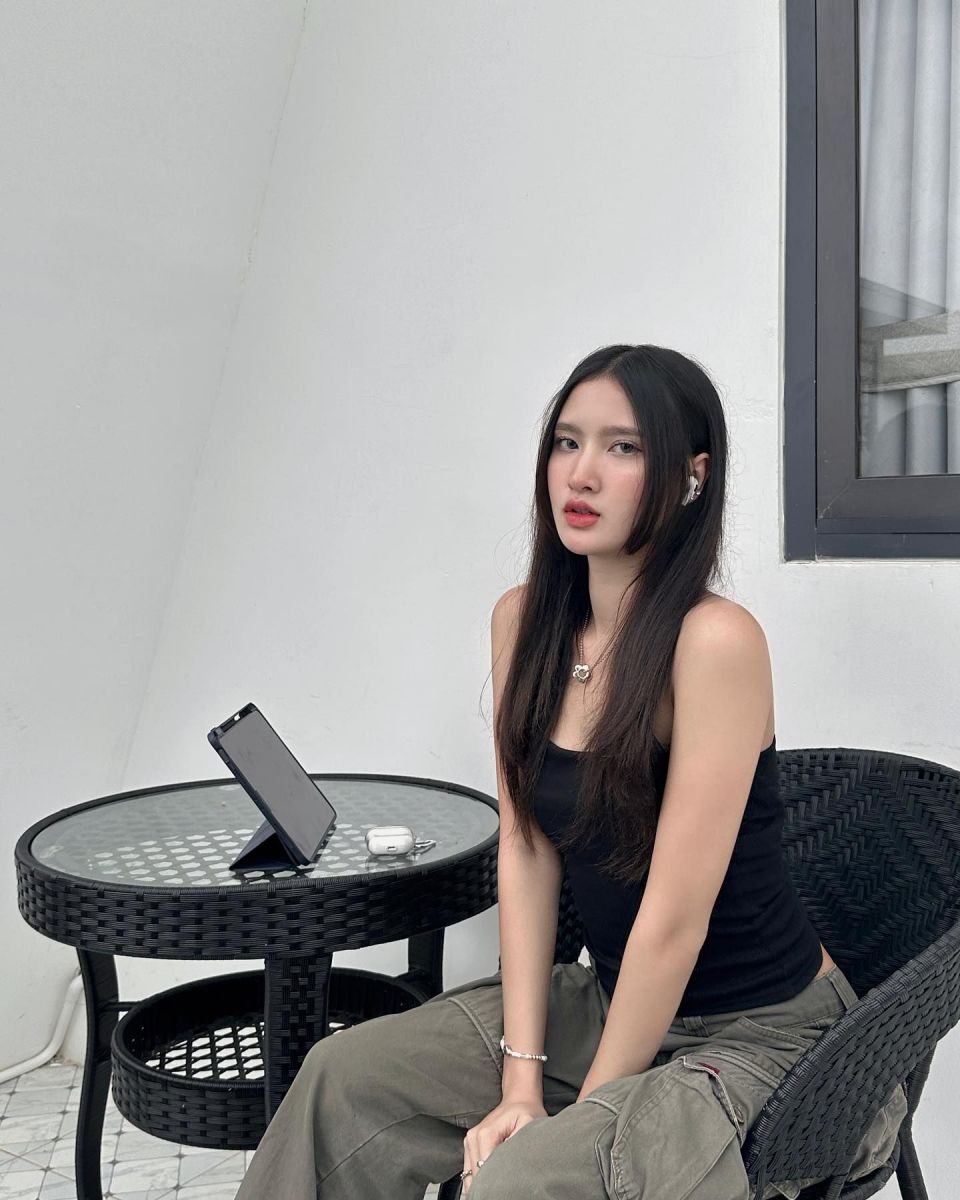 Cô gái trẻ mặc áo tank top đen và quần cargo xanh ngồi bên bàn trà