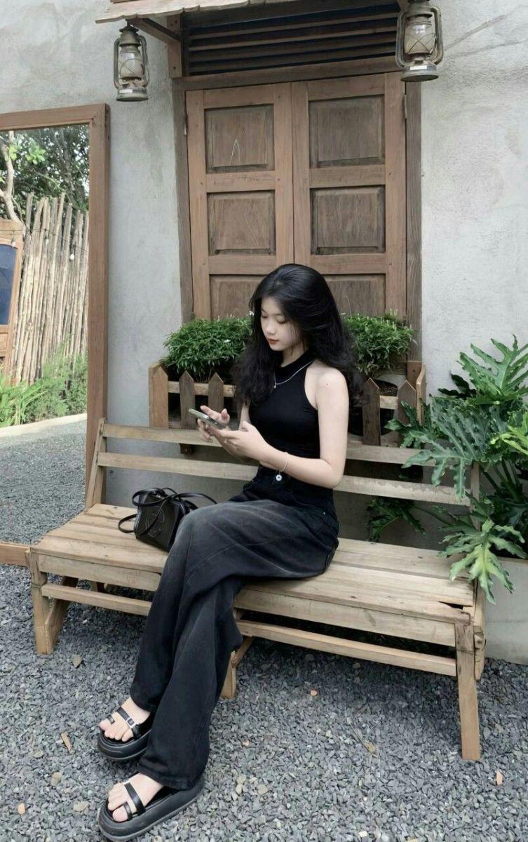 Cô gái trẻ mặc áo tank top đen và quần rộng ngồi trên ghế gỗ