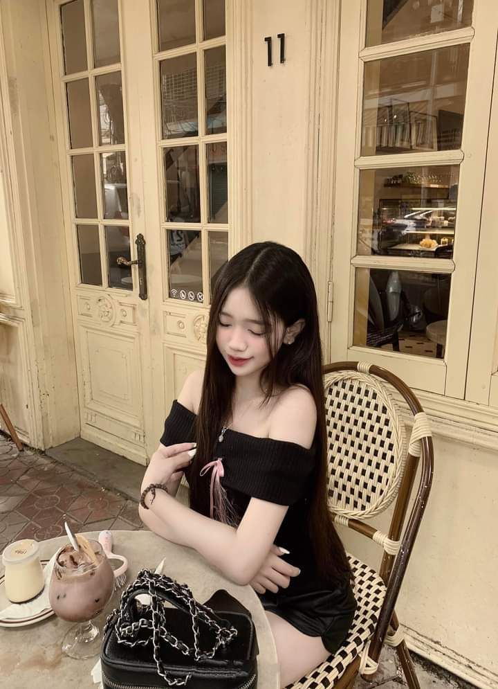 Cô gái trẻ mặc áo thun đen ngồi thưởng thức đồ uống tại quán cà phê