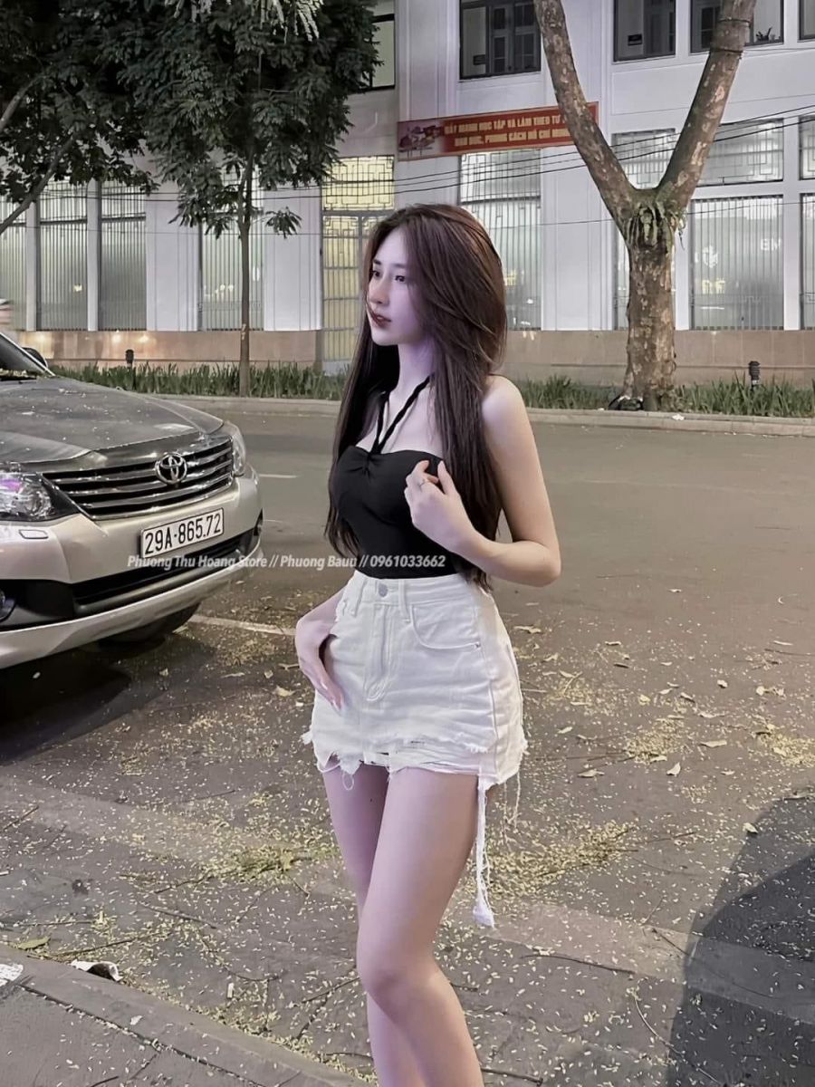 Cô gái trẻ mặc áo thun đen và chân váy ngắn trắng bên xe ô tô