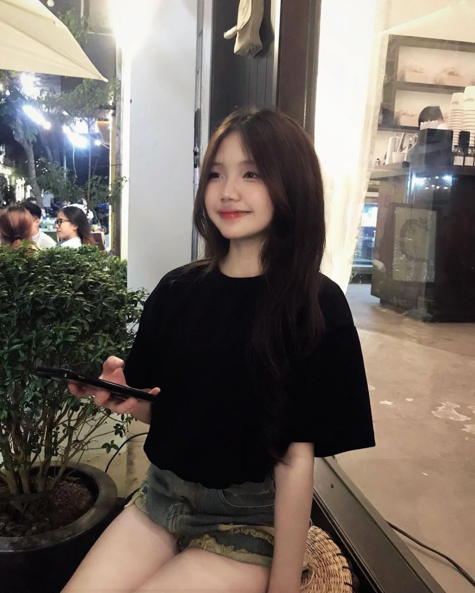 Cô gái trẻ mặc áo thun đen và quần sooc ngồi trên ghế tại quán cà phê