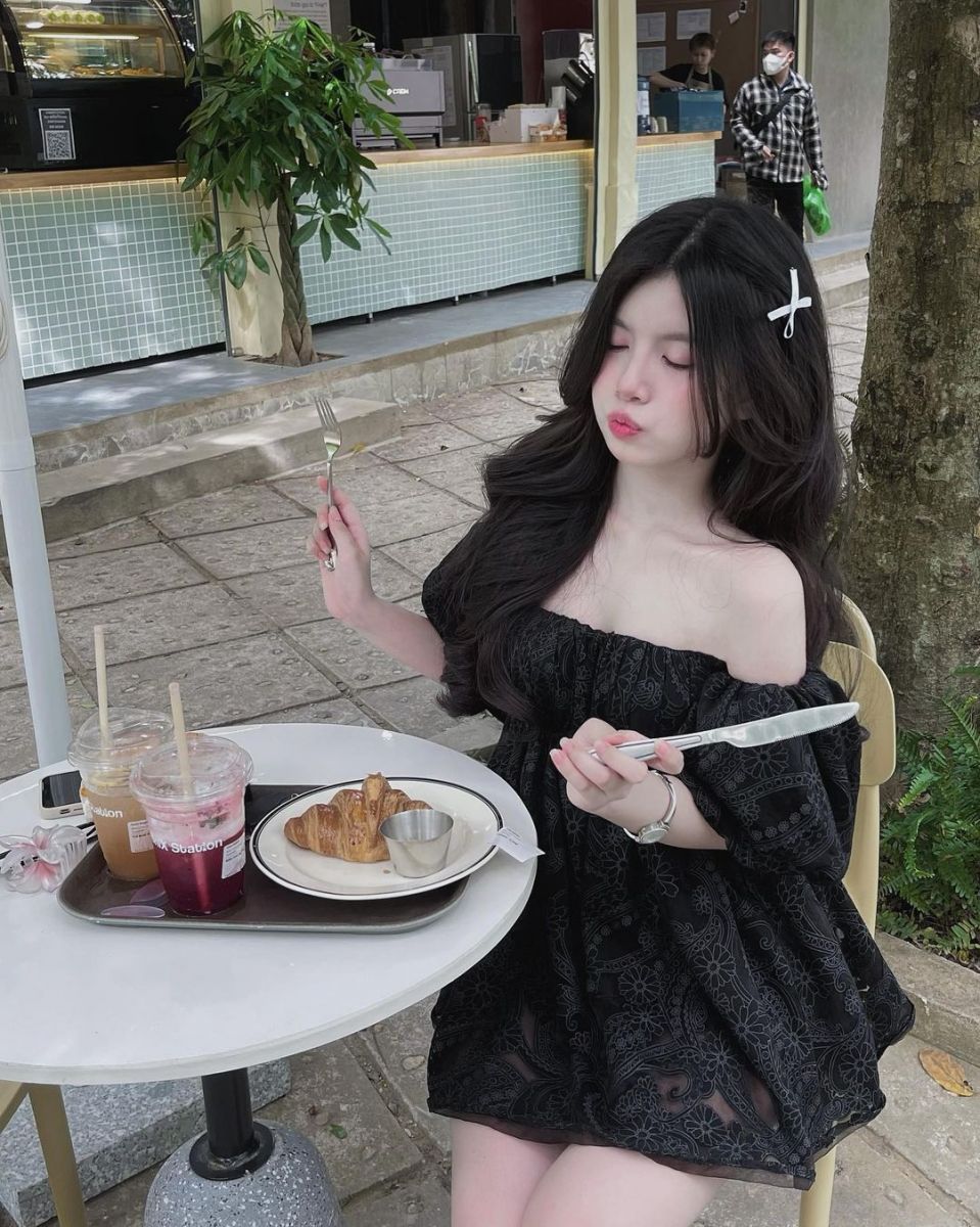 Cô gái trẻ mặc đầm đen ngồi tại quán cafe ngoài trời