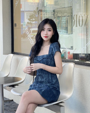 Cô gái trẻ mặc đầm jeans xanh ngồi trên ghế quán cà phê