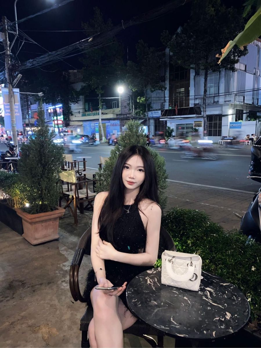 Cô gái trẻ mặc váy đen ngồi trên ghế cà phê ngoài trời