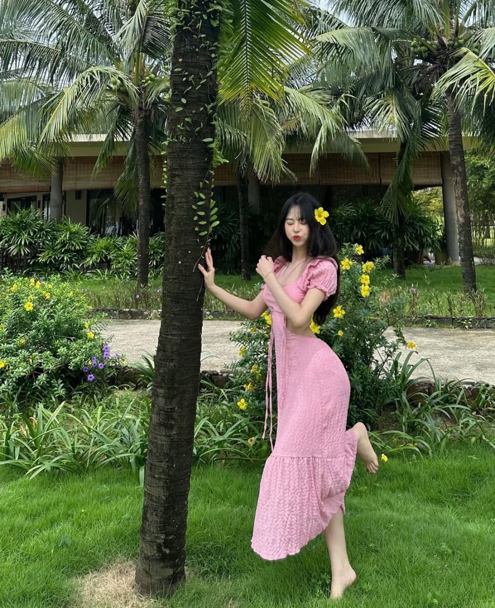 Cô gái trẻ mặc váy hồng tạo dáng vui vẻ trong khu vườn xanh tươi