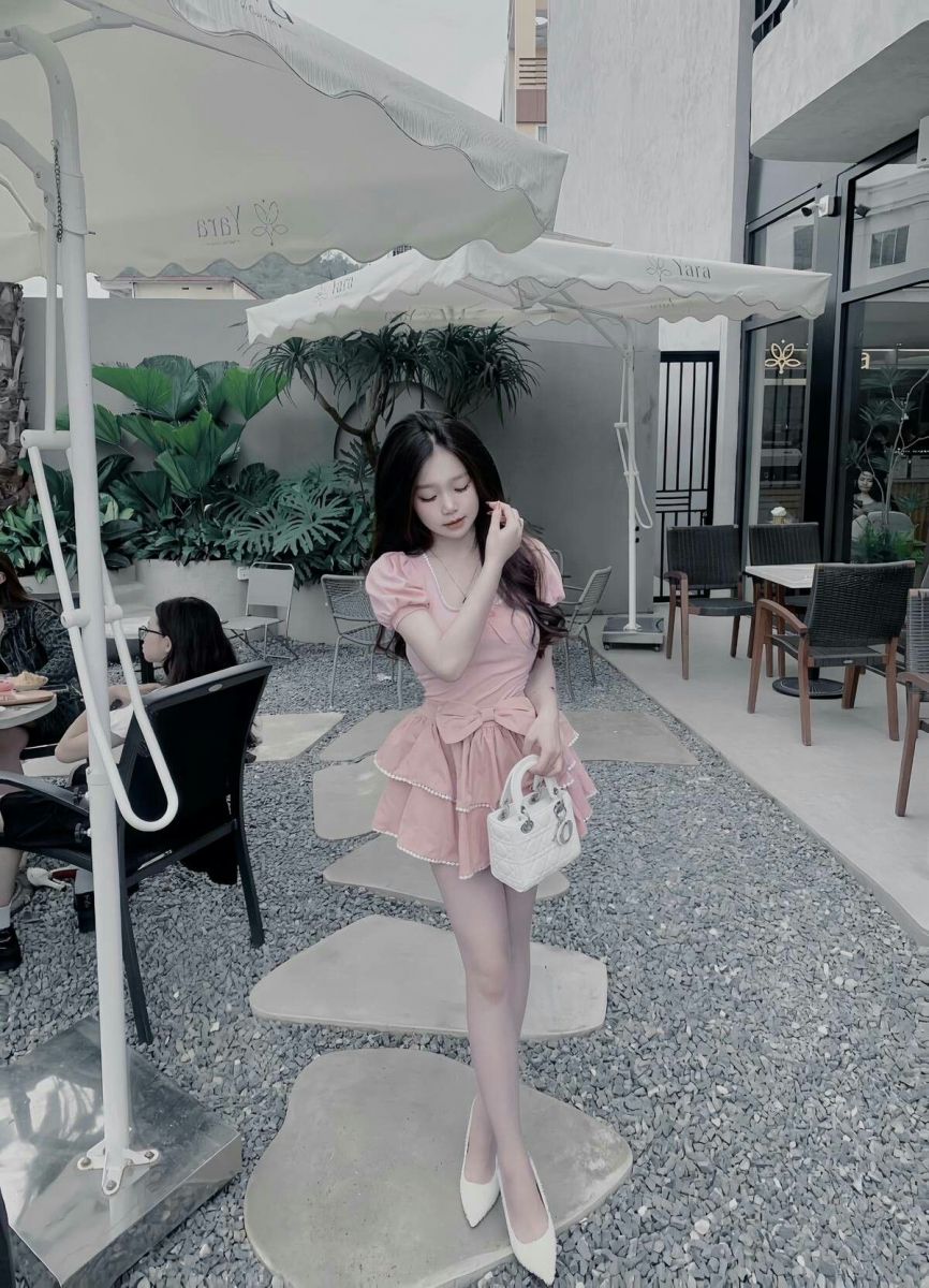 Cô gái trẻ mặc váy hồng xòe dịu dàng và túi xách trắng