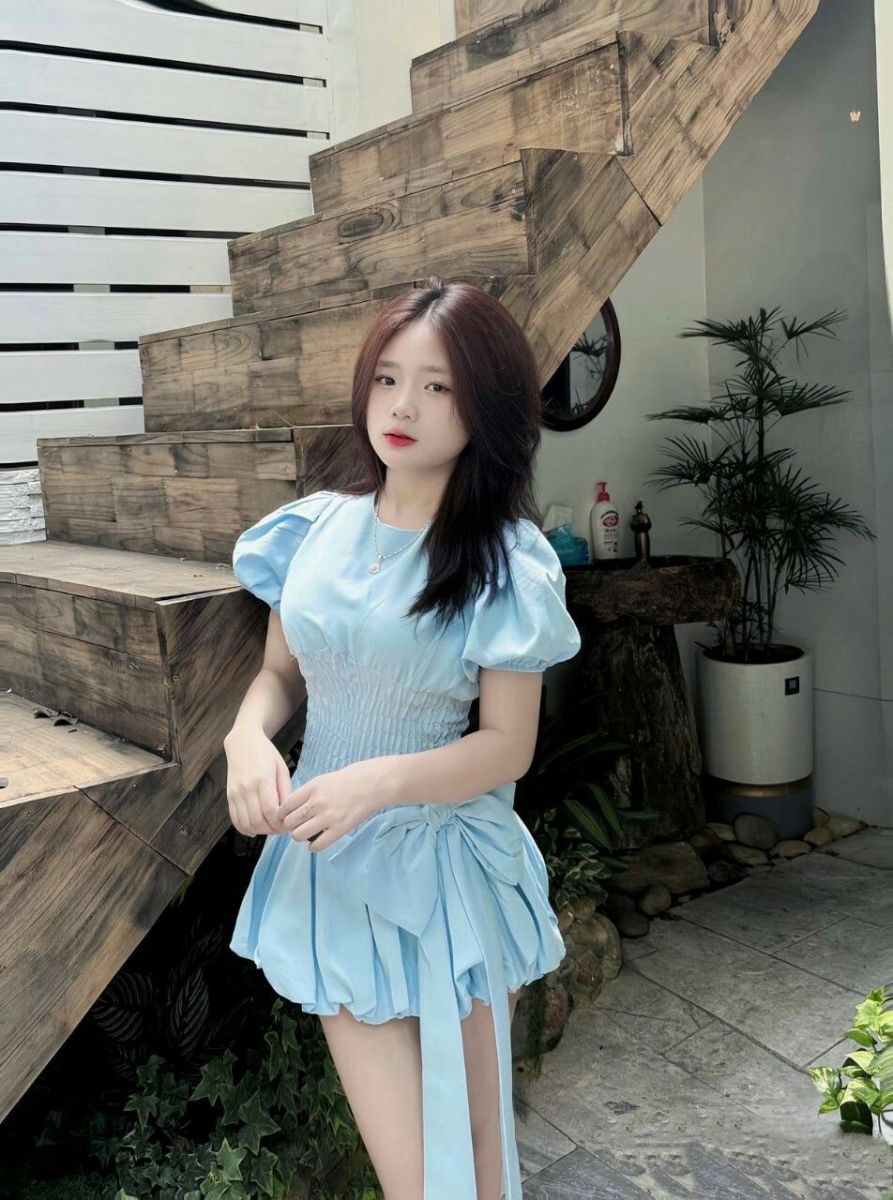 Cô gái trẻ mặc váy màu xanh nhạt bên cầu thang gỗ