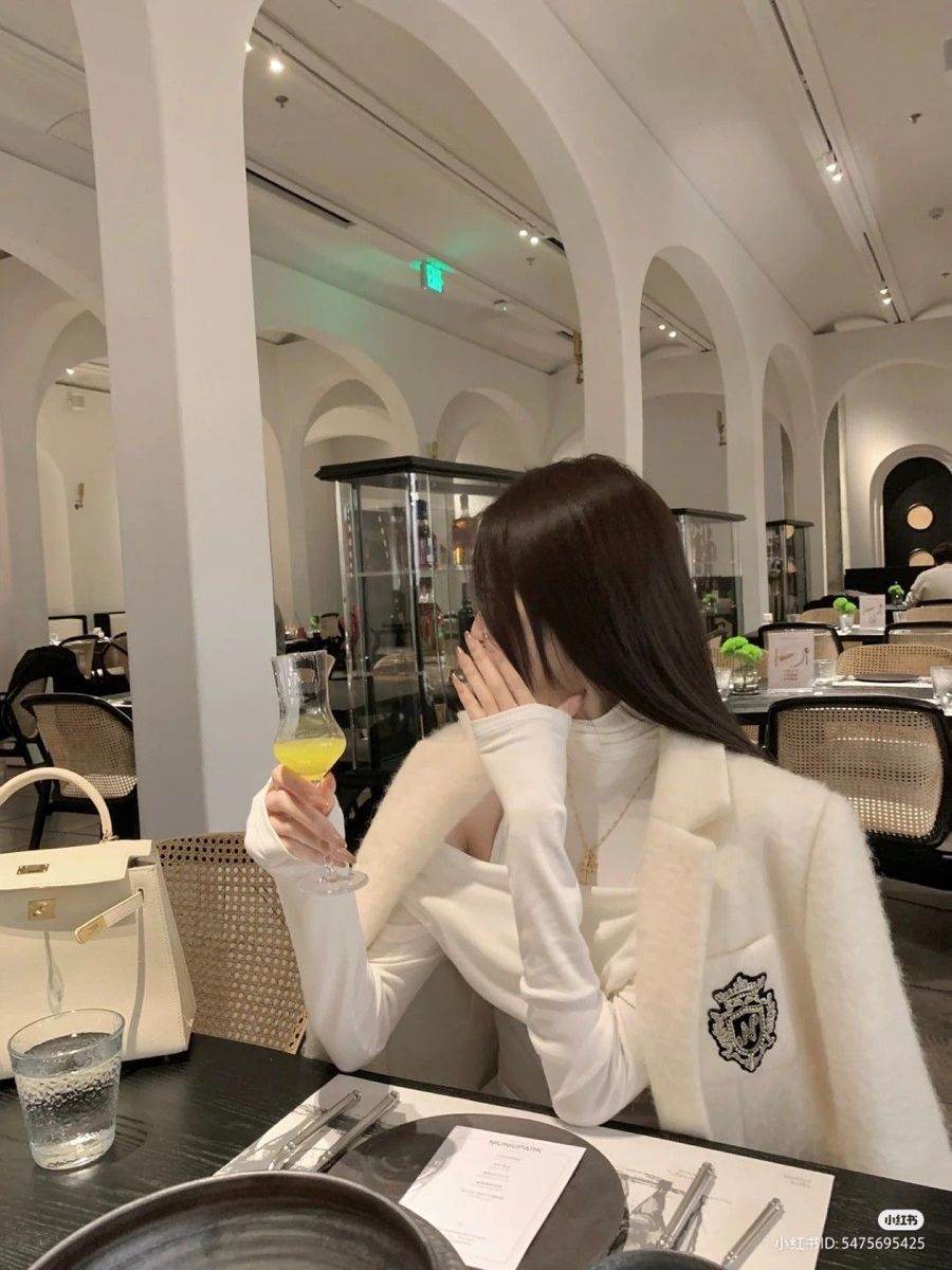 Cô gái trẻ trong áo khoác trắng cam, ngồi trong nhà hàng sang trọng
