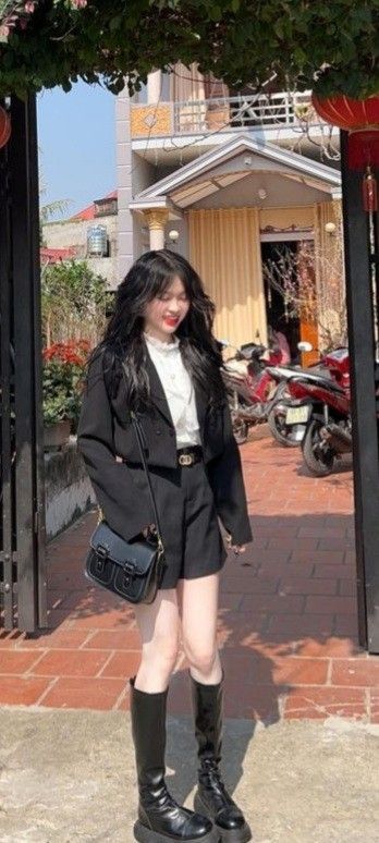 Cô gái trẻ trong bộ vest đen và áo trắng trước cổng nhà