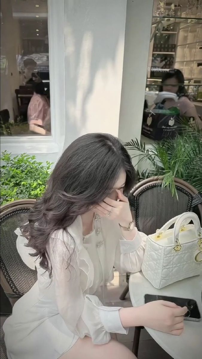 Cô gái trẻ trong chiếc áo blouse trắng ngồi ở quán cà phê