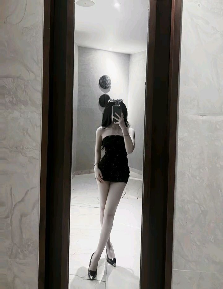 Cô gái trẻ trong váy ngắn màu đen trước gương sang trọng
