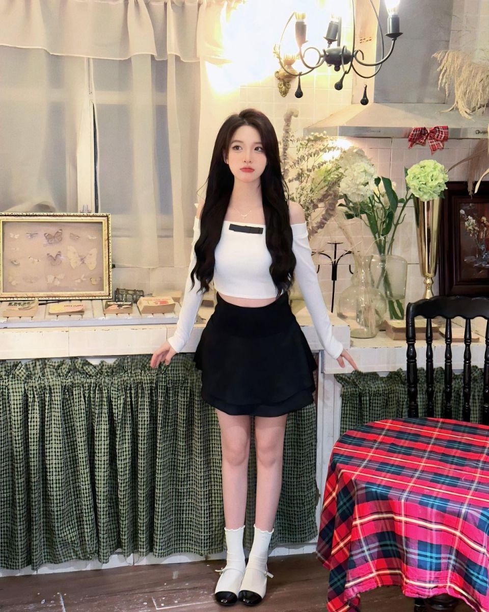 Cô gái trẻ với áo crop top trắng và chân váy đen trong không gian nội thất ấm cúng