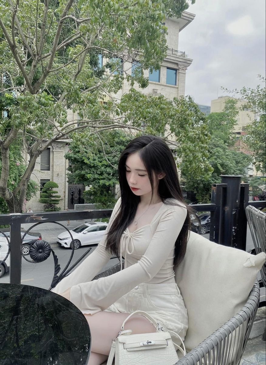Cô gái trẻ với áo sơ mi trắng và chân váy ngồi tại quán cafe