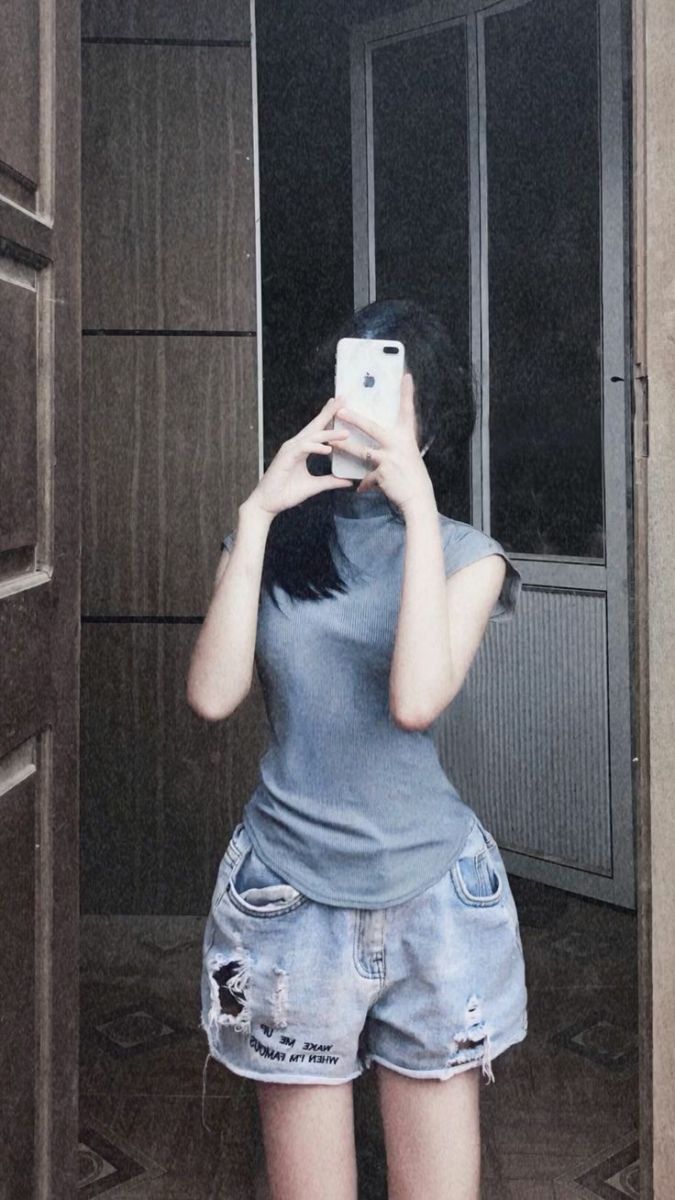 Cô gái trẻ xinh đẹp chụp ảnh selfie với áo thun xám và quần short jeans