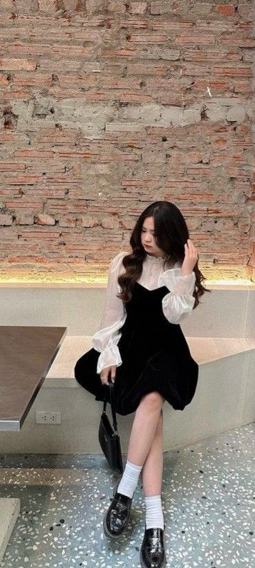 Cô gái trẻ xinh đẹp trong áo blouse trắng và váy đen tại quán cà phê