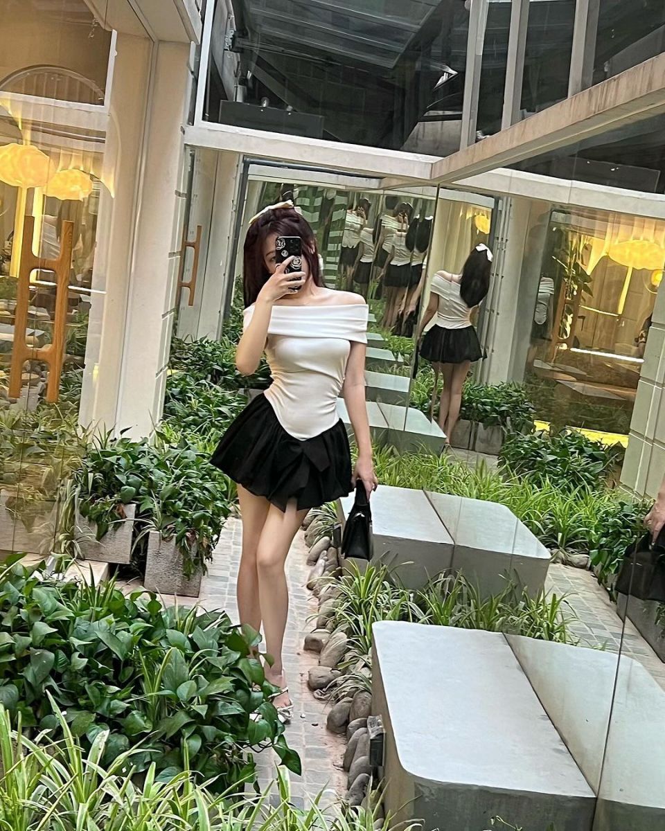 Cô gái trẻ xinh đẹp trong áo trắng và chân váy đen giữa khu vườn xanh