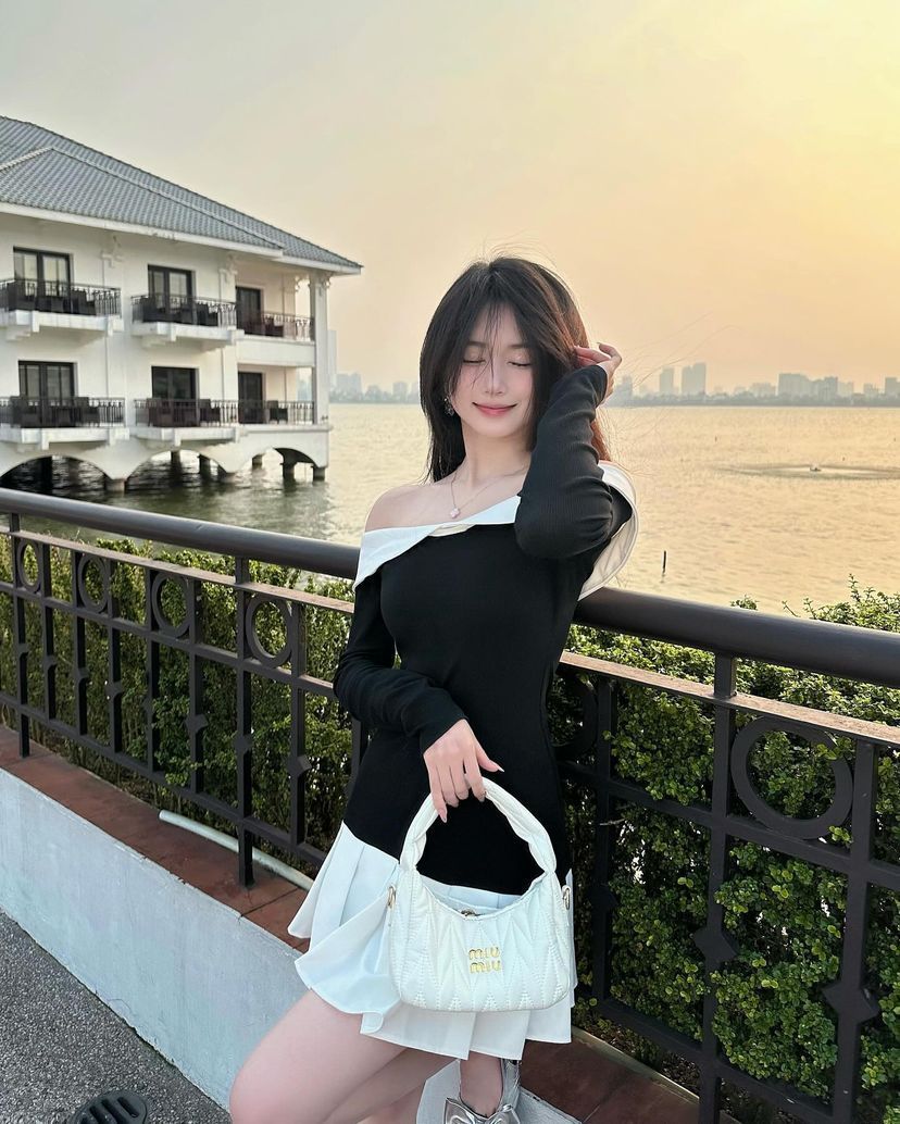 Cô gái trong áo dài tay màu đen và chân váy trắng bên dòng sông hoàng hôn