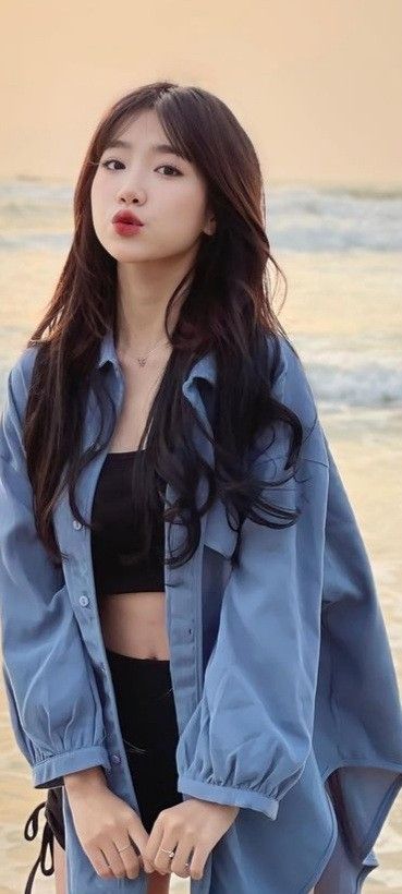 Cô gái xinh đẹp trong áo khoác xanh và áo crop top đen trên bãi biển