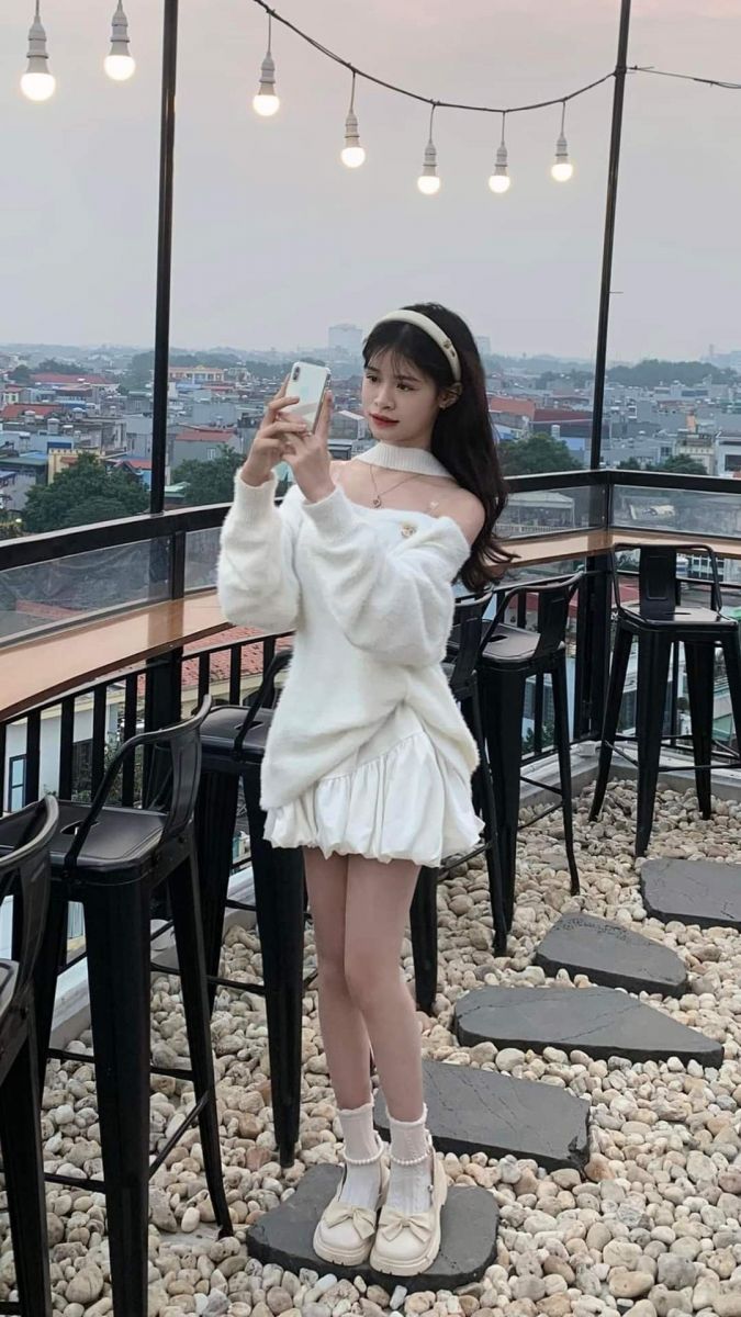 Cô gái xinh đẹp trong áo len trắng và váy trắng tại quán cà phê