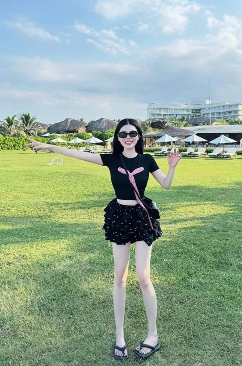Cô gái xinh đẹp trong áo thun đen và chân váy xòe trên bãi cỏ xanh