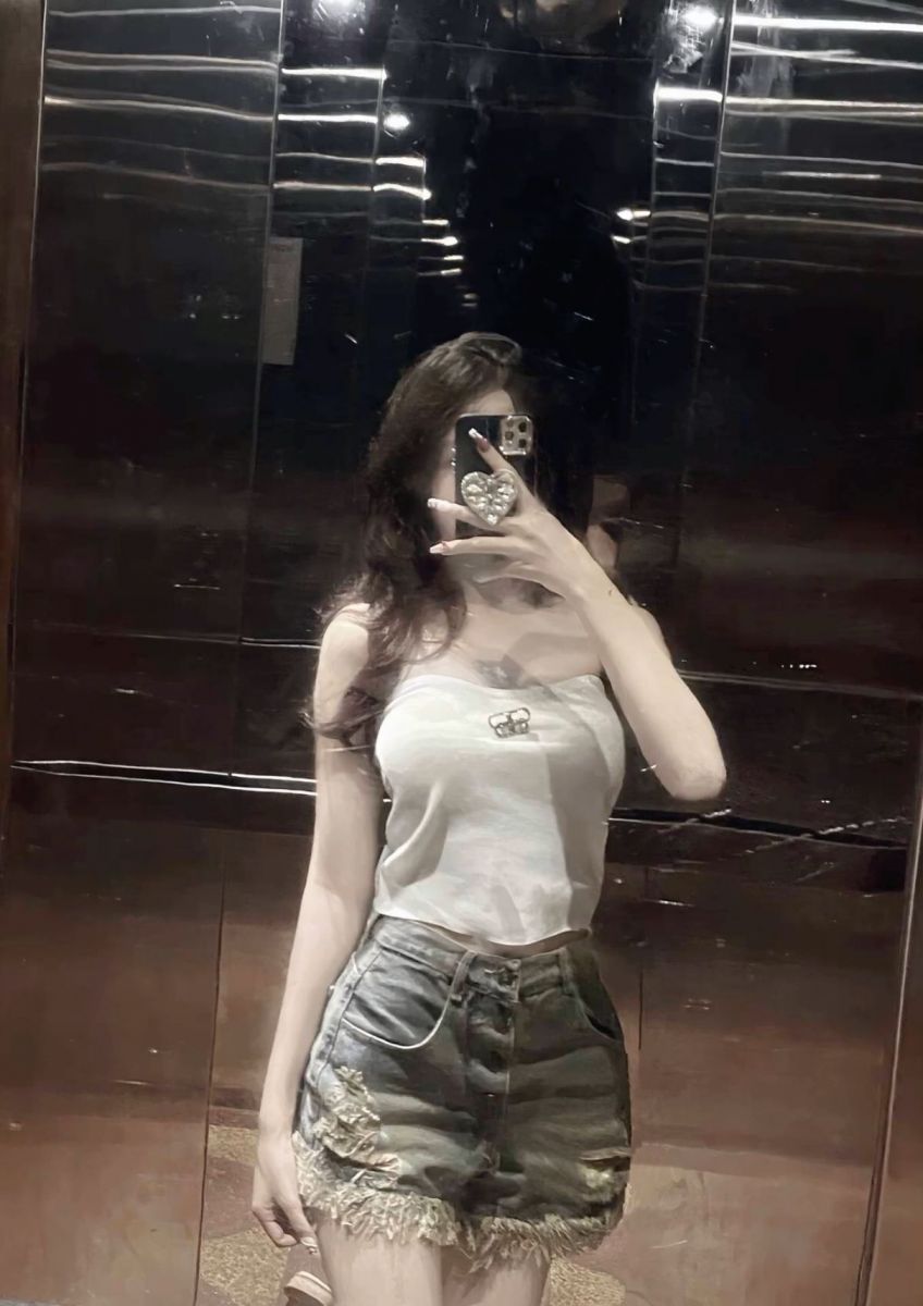Cô gái xinh đẹp trong thang máy với áo ba lô trắng và quần shorts jeans rách