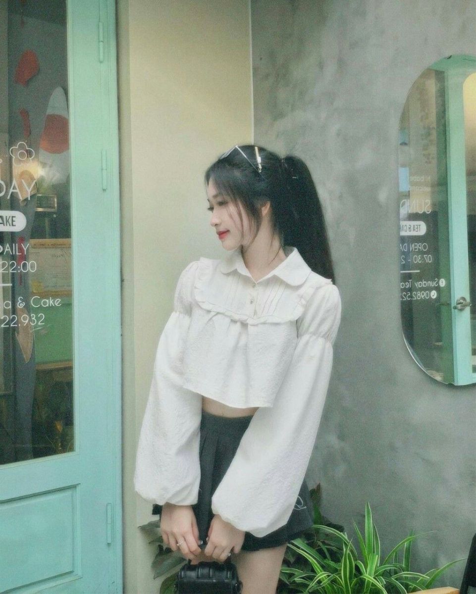 Cô gái xinh mặc áo crop top trắng và chân váy đen bên quán cà phê