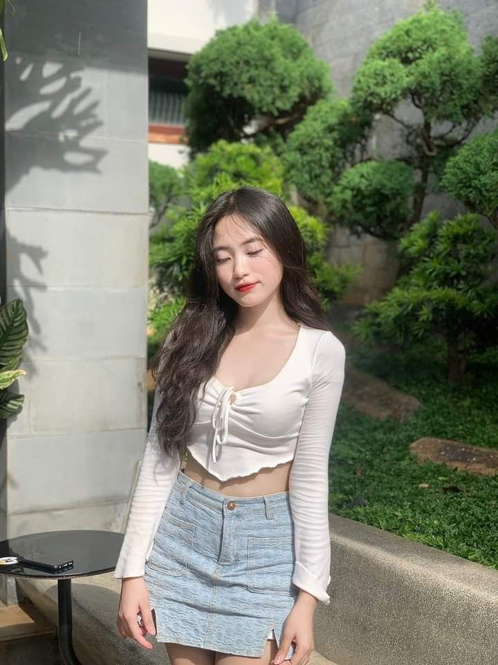 Cô gái xinh mặc áo crop trắng và chân váy denim trong khu vườn xanh mát