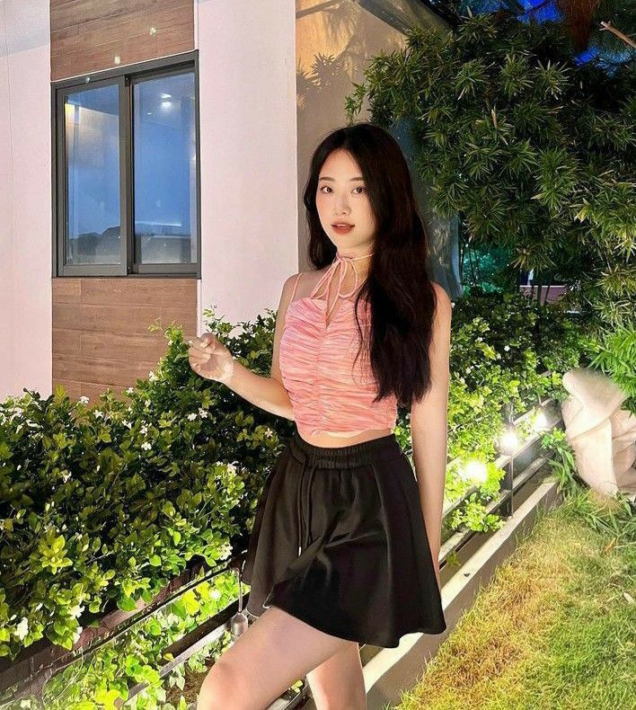 Cô gái xinh mặc áo hai dây màu hồng và chân váy đen trong khung cảnh xanh tươi
