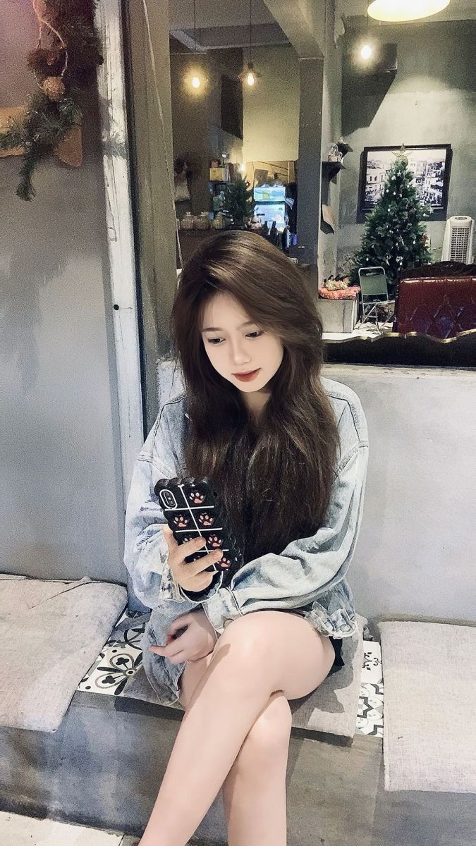 Cô gái xinh mặc áo khoác denim ngồi trên ghế đưa điện thoại