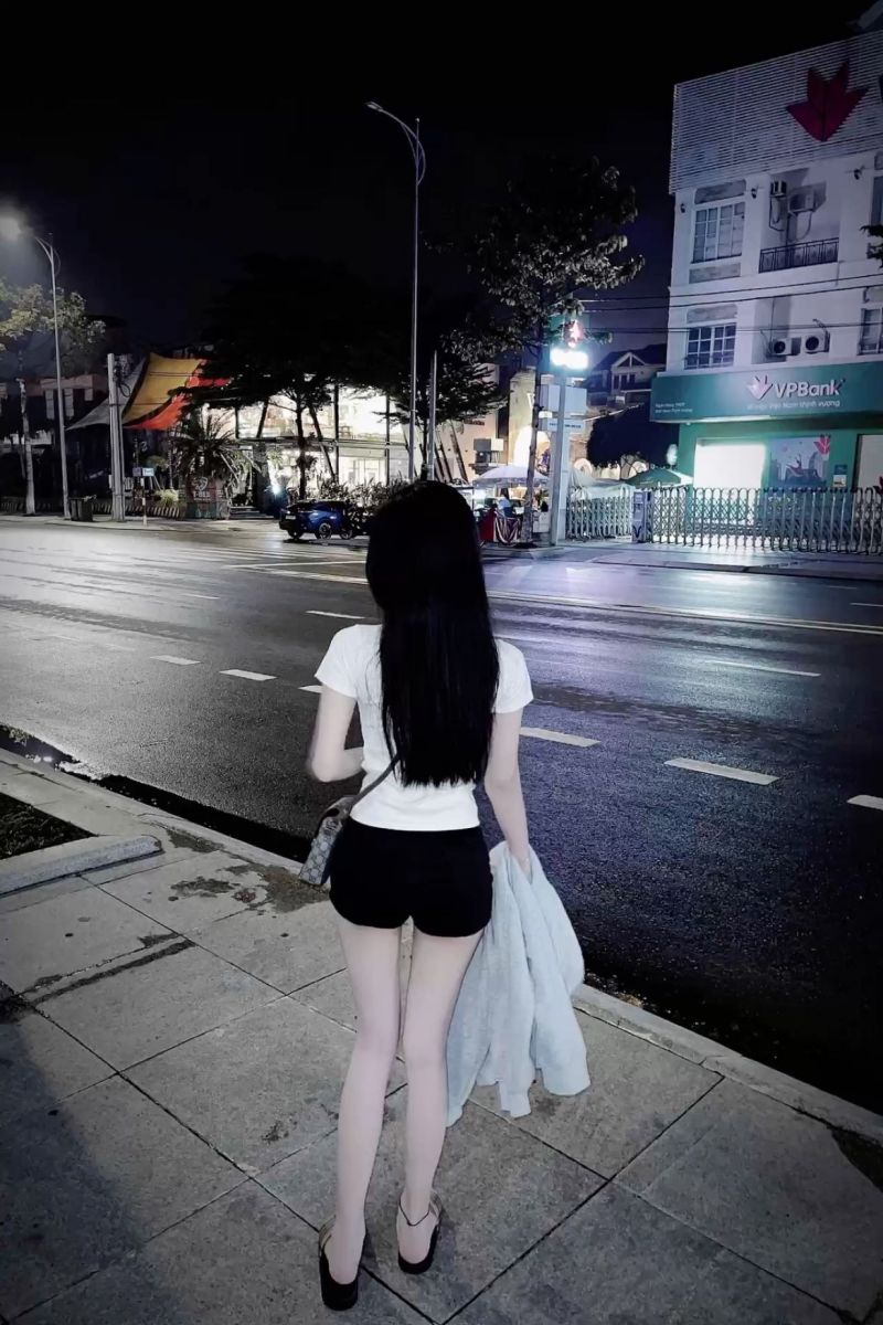Cô gái xinh mặc áo thun trắng và quần sọc đen bên lề đường