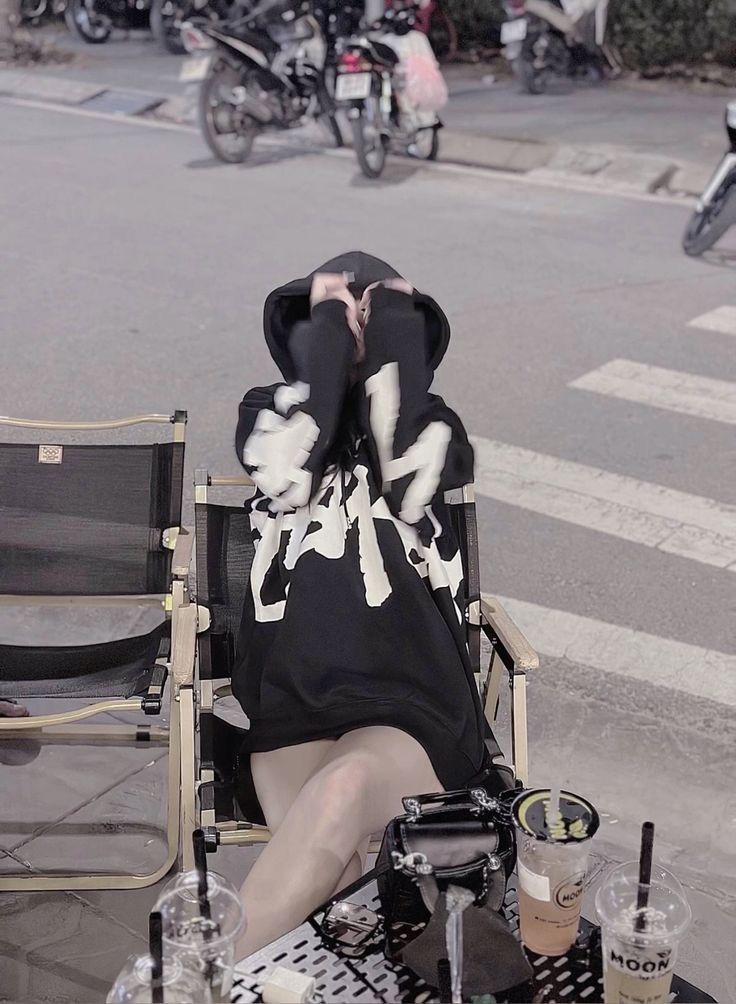 Gái che mặt ngồi trên ghế ngoài trời với áo hoodie đen