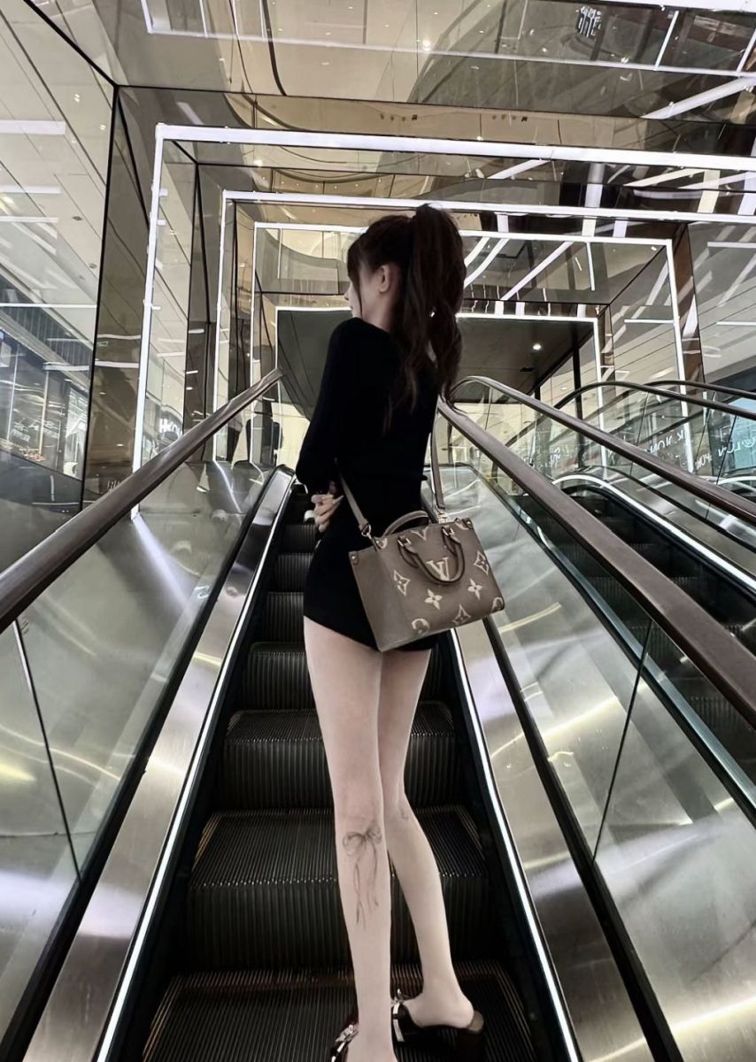 Gái đẹp mặc áo khoác đen và váy ngắn trên thang cuốn