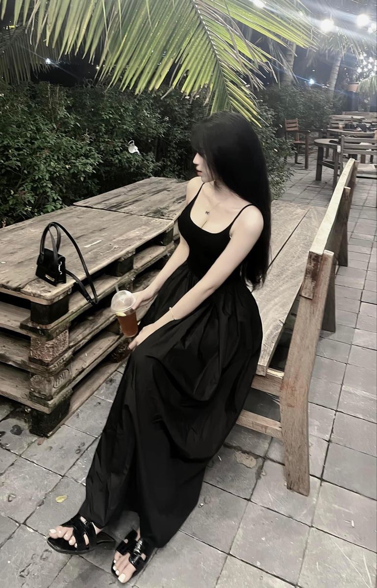 Gái đẹp mặc váy đen dài ngồi thư giãn tại quán cà phê ngoài trời