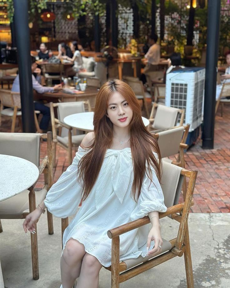 Gái đẹp mặc váy trắng ngồi trên ghế gỗ tại quán cà phê